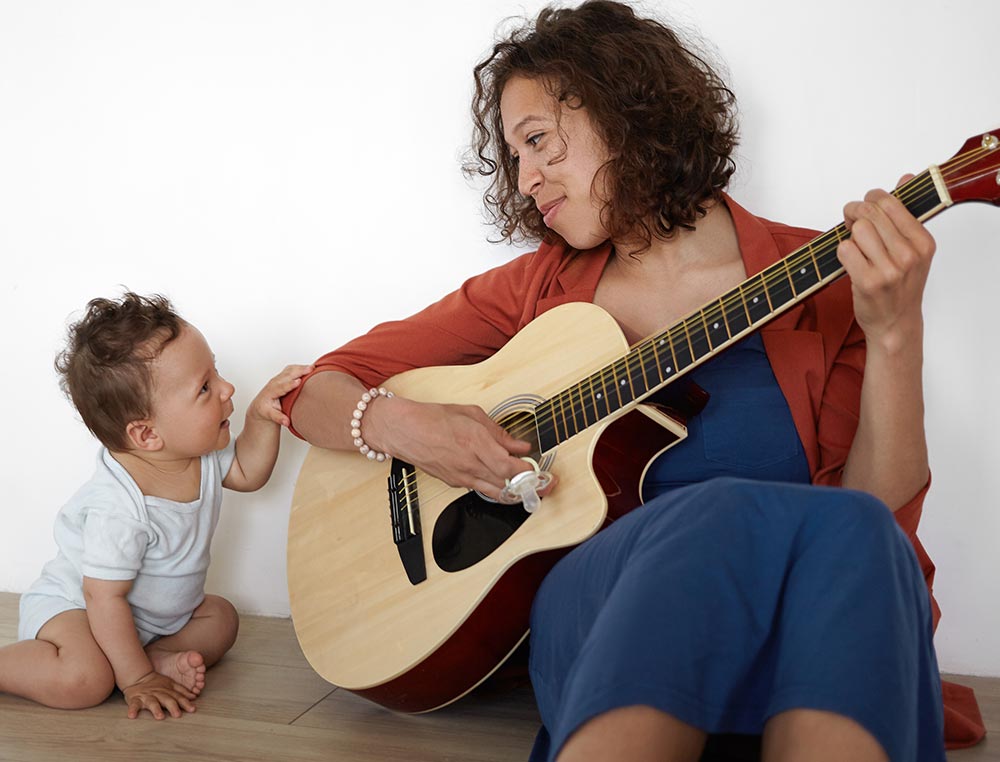 A lady playing guitar next to her infant child